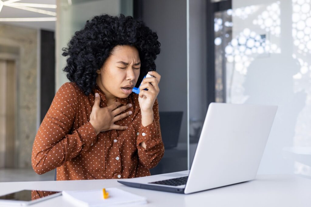 Young woman using inhaler for asthma relief at work